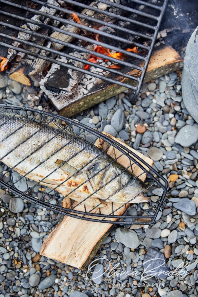 overhead view of cooking sea bass over open fire on the beach