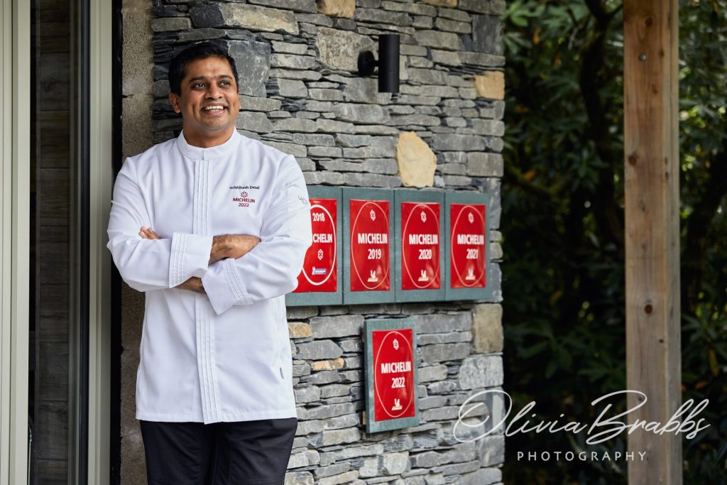 Michelin starred chef Hrishikesh Desai standing my Michelin plaques outside the kitchen at The Gilpin Hotel in the Lake District
